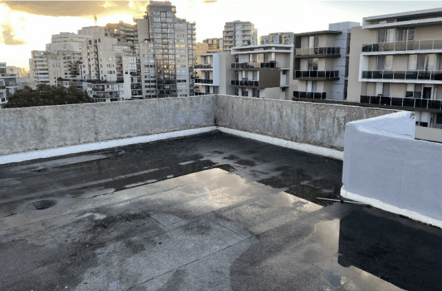Flat roof with standing water along parapet walls before waterproofing at Bondi Junction